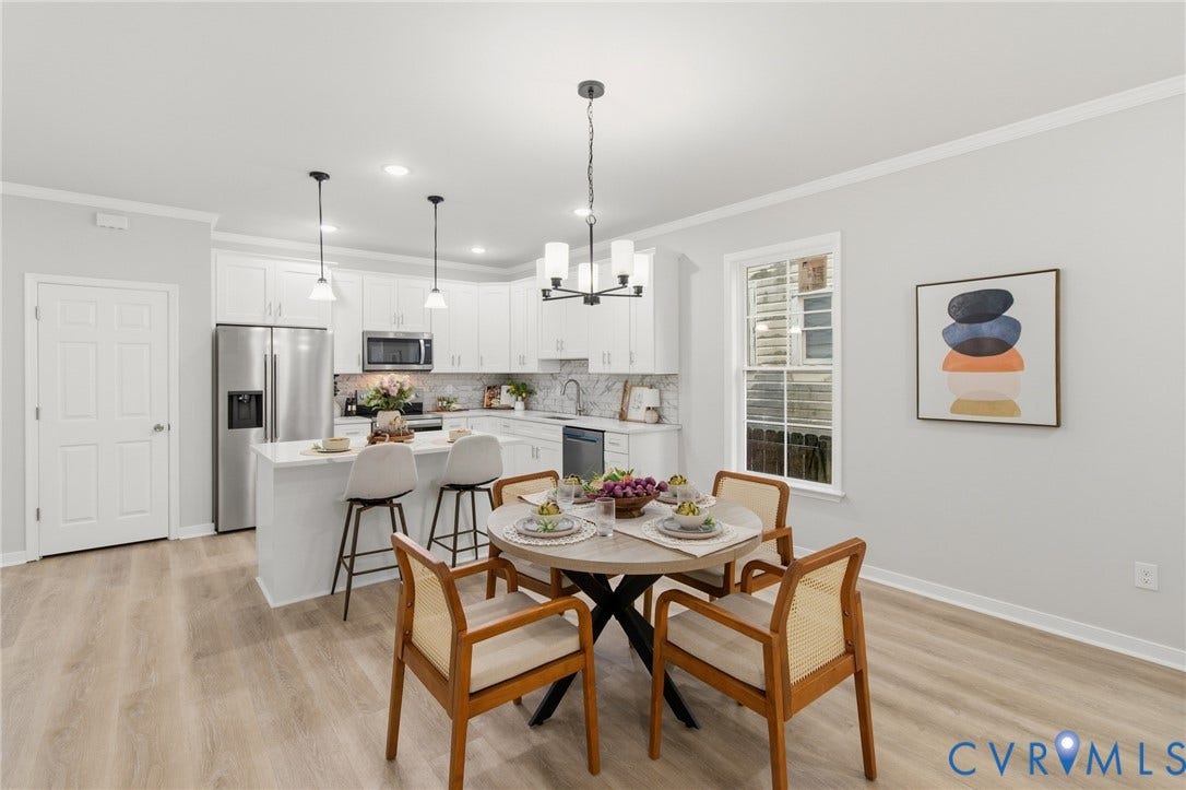 Open-concept living space with wood-finish flooring, a kitchen island, white cabinetry, and stainless steel appliances