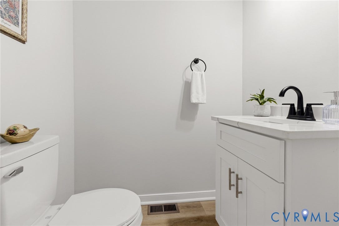White vanity with a solid surface countertop, matte black faucet, and wood-finish flooring