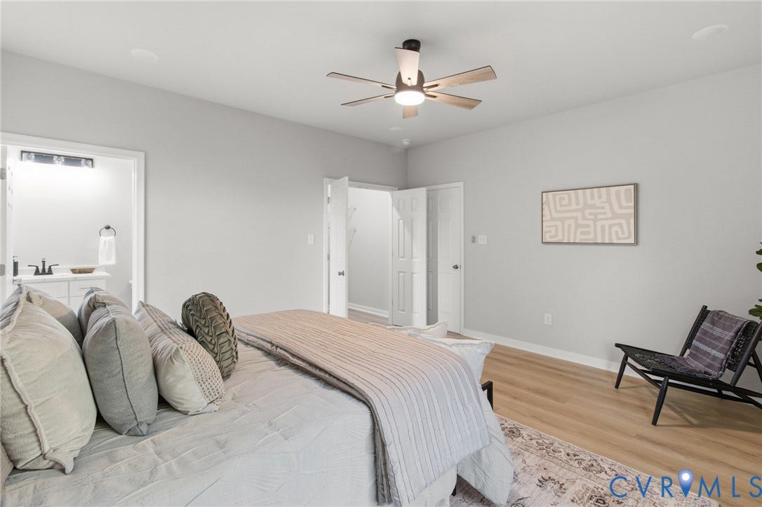 Light-toned wood-finish flooring, ceiling fan with integrated lighting, and an entryway to a full bathroom featuring a vanity with a rectangular basin sink and a wall-mounted light fixture