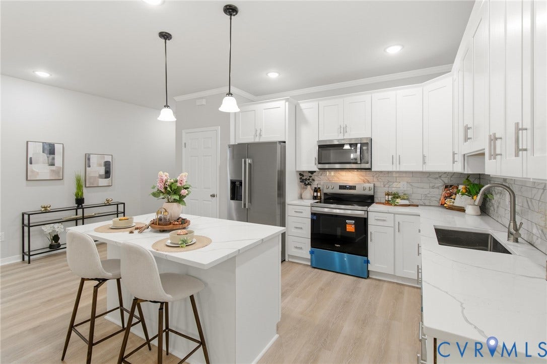 Open-concept kitchen featuring an island with seating, white shaker cabinetry, stainless steel appliances, and a tile backsplash
