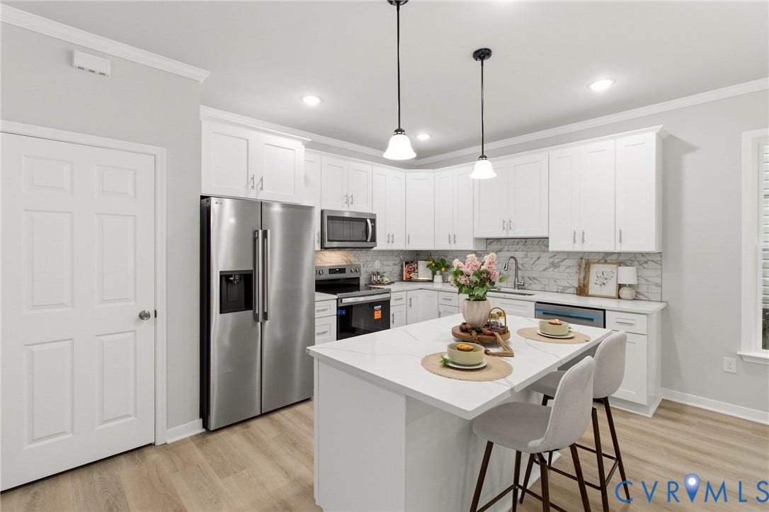 White shaker cabinetry, stainless steel appliances, central island with seating, pendant lighting, and wood-finish flooring