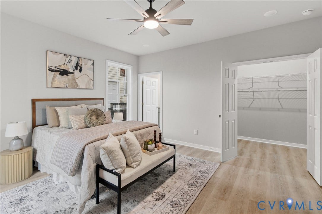 Light-toned wood-finish flooring, ceiling fan with integrated lighting, window with white trim, double bi-fold closet doors, and built-in wire shelving
