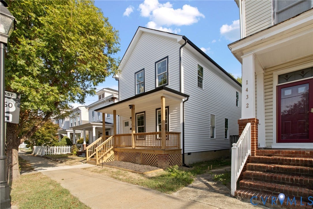 White siding exterior with a covered wooden porch, black-trimmed windows, and a dark roof
