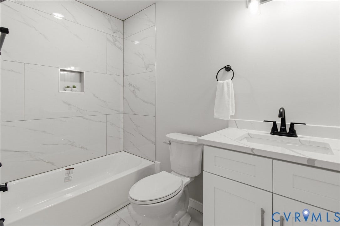 White subway tile shower surround with a built-in niche, white bathtub, white vanity with integrated sink, matte black faucet, and white tile flooring