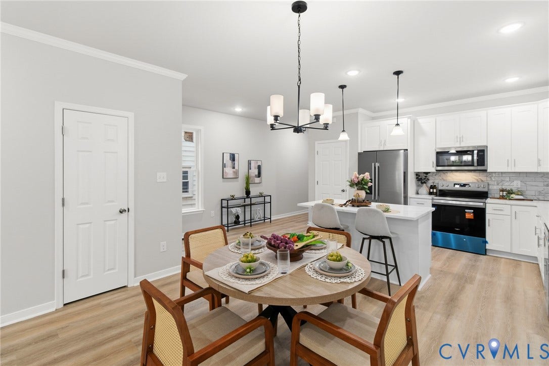 Open-concept living space with wood-finish flooring, white cabinetry, a kitchen island with seating, pendant lighting, and stainless steel appliances