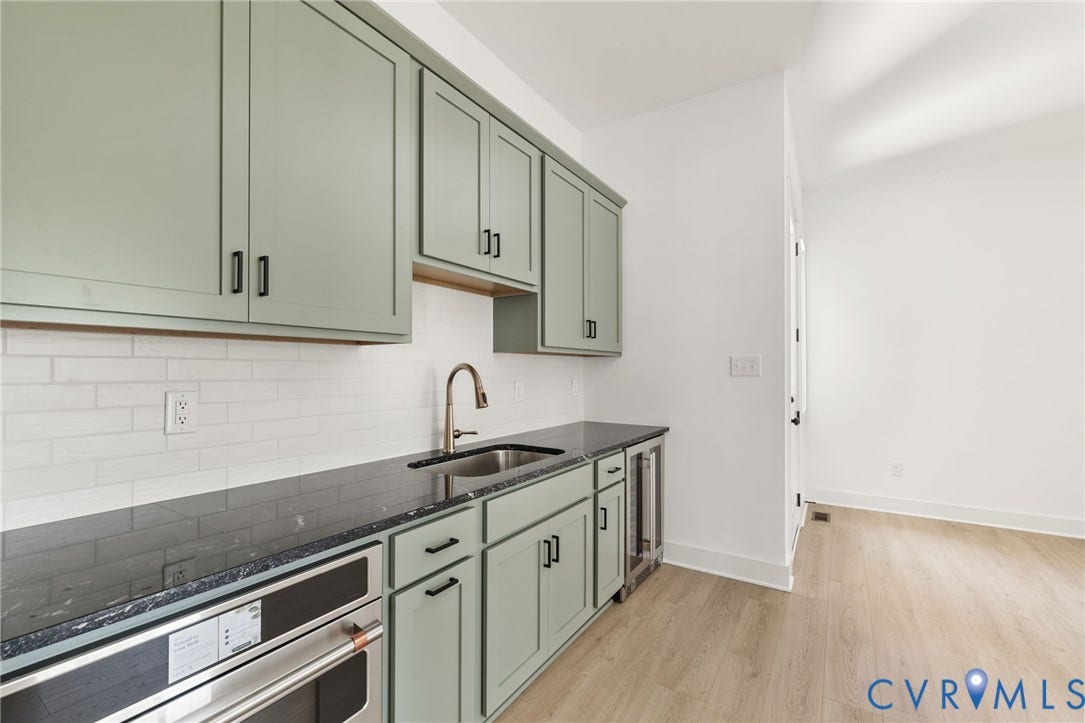 9514 Angels Share Drive, New Kent, VA 23141 Light green shaker-style cabinetry with black hardware, dark stone countertops, white subway tile backsplash, and a built-in stainless steel beverage cooler