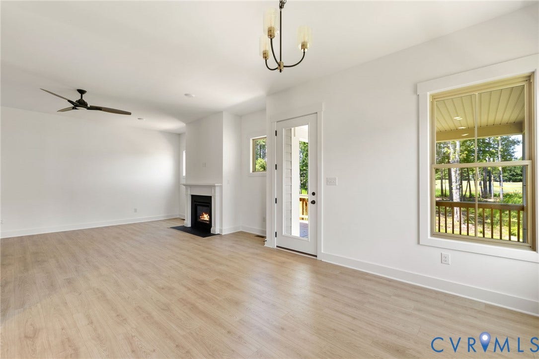 9514 Angels Share Drive, New Kent, VA 23141 Open-concept living space featuring wood-finish flooring, a white mantel fireplace with a black surround, a ceiling fan, and a glass-paneled door