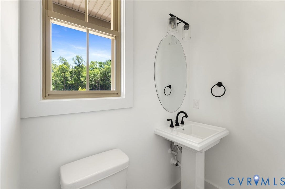9514 Angels Share Drive, New Kent, VA 23141 Pedestal sink with black hardware, oval mirror, and window with natural scenery