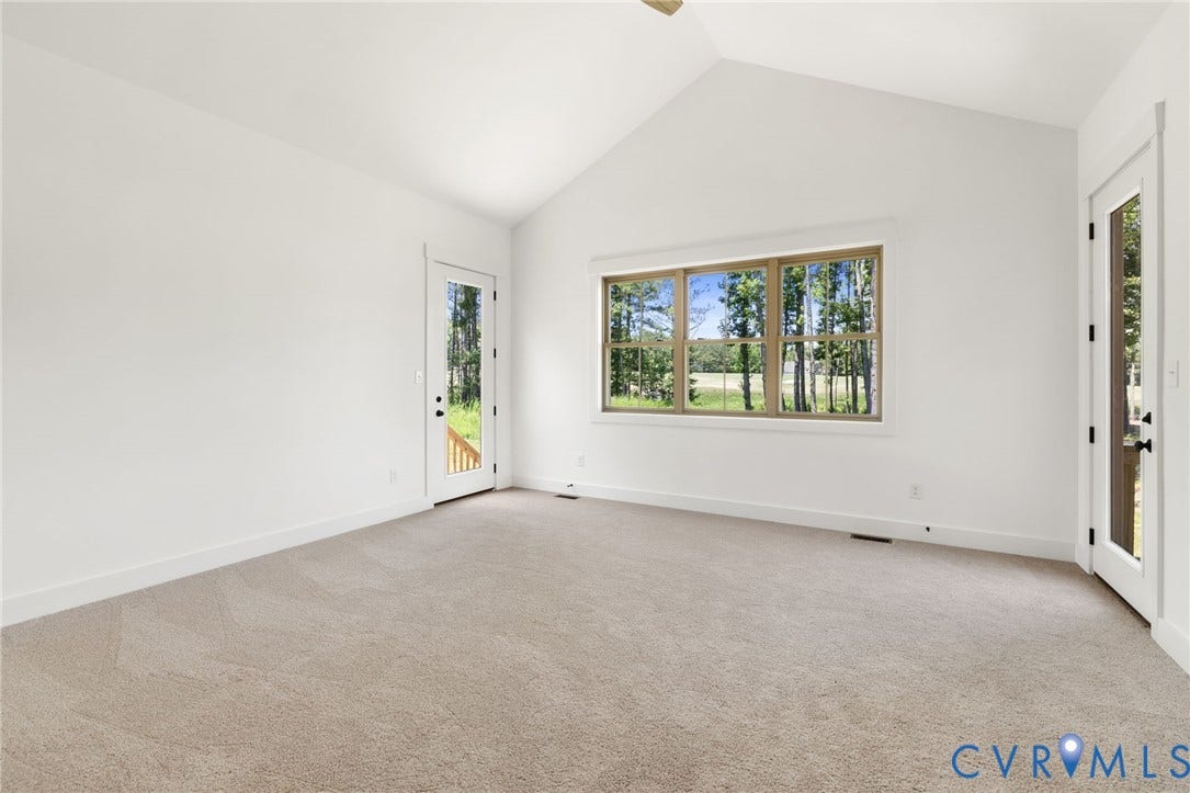 9514 Angels Share Drive, New Kent, VA 23141 Vaulted ceiling with a ceiling fan, carpeted flooring, large window with wood-finish trim, and two glass-paneled doors providing exterior access