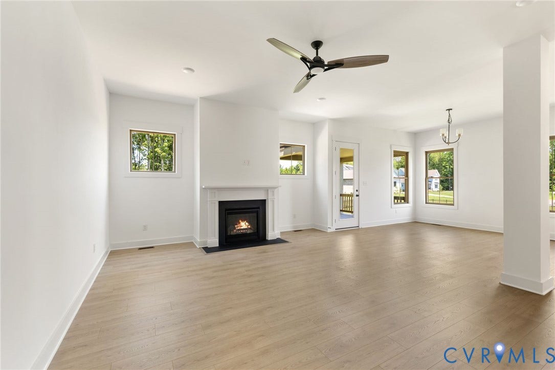 9514 Angels Share Drive, New Kent, VA 23141 Expansive room featuring wood-finish flooring, a contemporary ceiling fan, and a fireplace with a white mantel and dark hearth