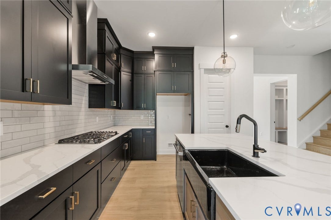 9514 Angels Share Drive, New Kent, VA 23141 Black cabinetry, white subway tile backsplash, white countertops, built-in gas range with stainless steel hood, and a kitchen island with an integrated sink and matte black faucet