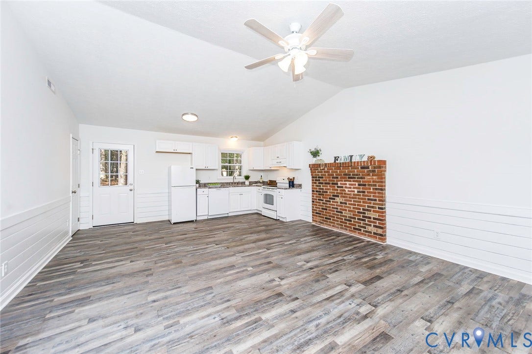 21108 Matoaca Road, Chesterfield, VA 23803 Vaulted ceiling with a ceiling fan, wood-finish flooring, white shiplap paneling, brick accent wall, and a kitchen with white cabinetry and appliances
