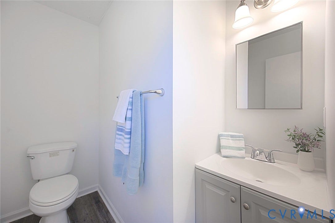21108 Matoaca Road, Chesterfield, VA 23803 White toilet, wood-finish flooring, gray vanity with silver hardware, integrated sink, and wall-mounted mirror