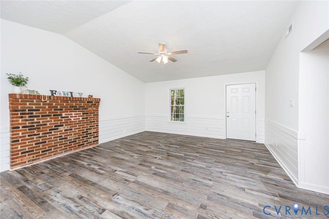 21108 Matoaca Road, Chesterfield, VA 23803 Vaulted ceiling, wood-finish flooring, white shiplap wainscoting, brick fireplace, and a ceiling fan with integrated lighting