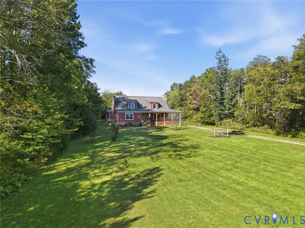 16233 Pleasant Mill Road, Montpelier, VA 23192 Two-story residence featuring a covered front porch, dormer windows, and a shingle roof, set on a sprawling grass lot surrounded by mature trees