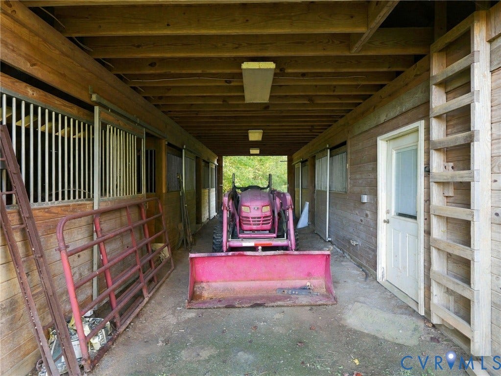 16233 Pleasant Mill Road, Montpelier, VA 23192 Covered stable area featuring wood-paneled walls, exposed wood ceiling joists, vertical metal stall partitions, and an integrated exterior door