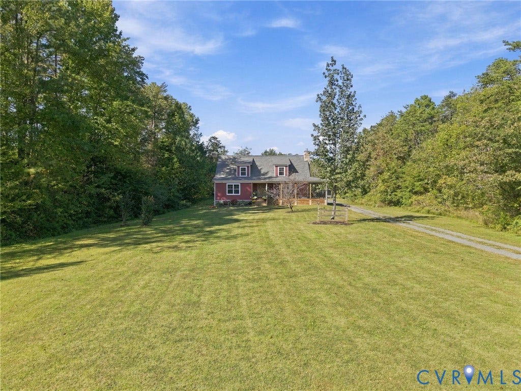 16233 Pleasant Mill Road, Montpelier, VA 23192 Cape Cod-style residence featuring a covered front porch, dormer windows, and a gravel driveway situated on a large, grass-covered lot surrounded by mature trees
