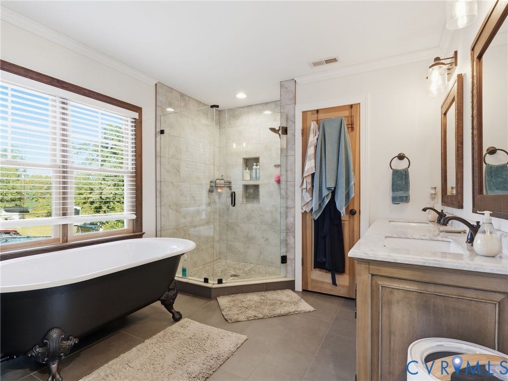16233 Pleasant Mill Road, Montpelier, VA 23192 Freestanding clawfoot tub, dual-sink vanity with stone countertop, walk-in glass-enclosed shower featuring tile surround and built-in recessed shelving, and dark-toned cabinetry