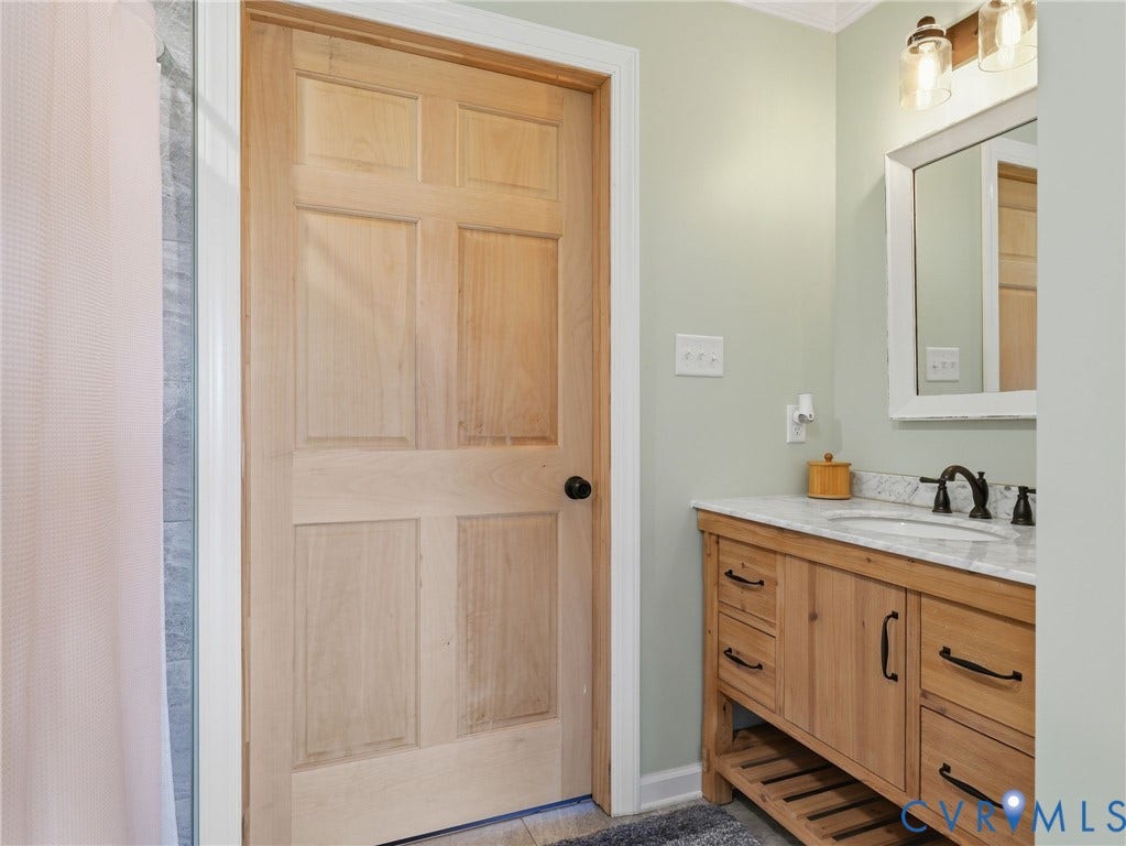 16233 Pleasant Mill Road, Montpelier, VA 23192 Bathroom featuring a natural wood-finish vanity with stone-top surfacing, undermount sink, matte black hardware, and matching solid wood six-panel door