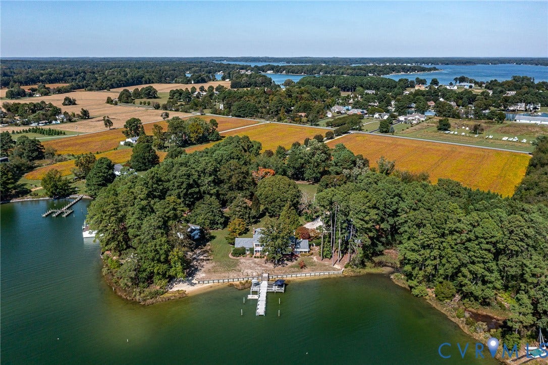 Waterfront property with multiple private docks, a sandy shoreline, a tree-lined perimeter, and surrounding agricultural fields