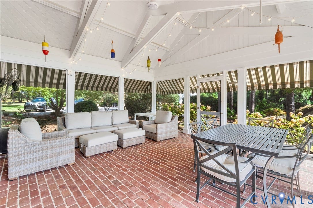 Screened porch featuring a vaulted white ceiling, exposed beams, brick flooring, and retractable striped awnings. Beautiful views of water