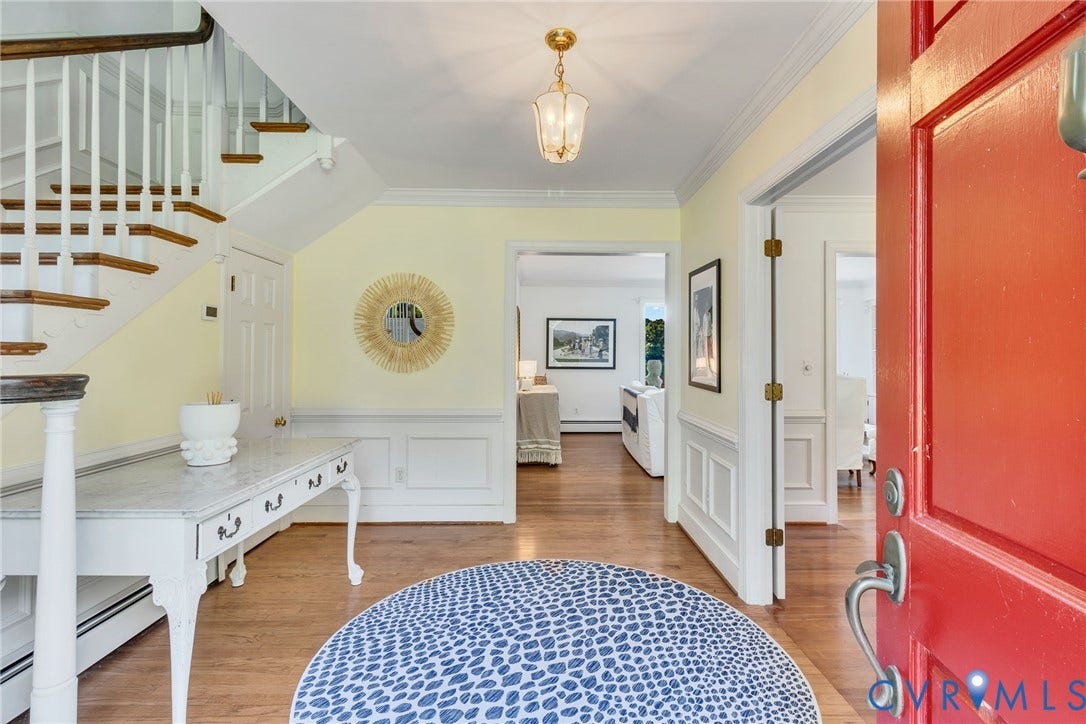 Hardwood flooring throughout, a prominent staircase with white balusters, wainscoting, and a decorative overhead light fixture