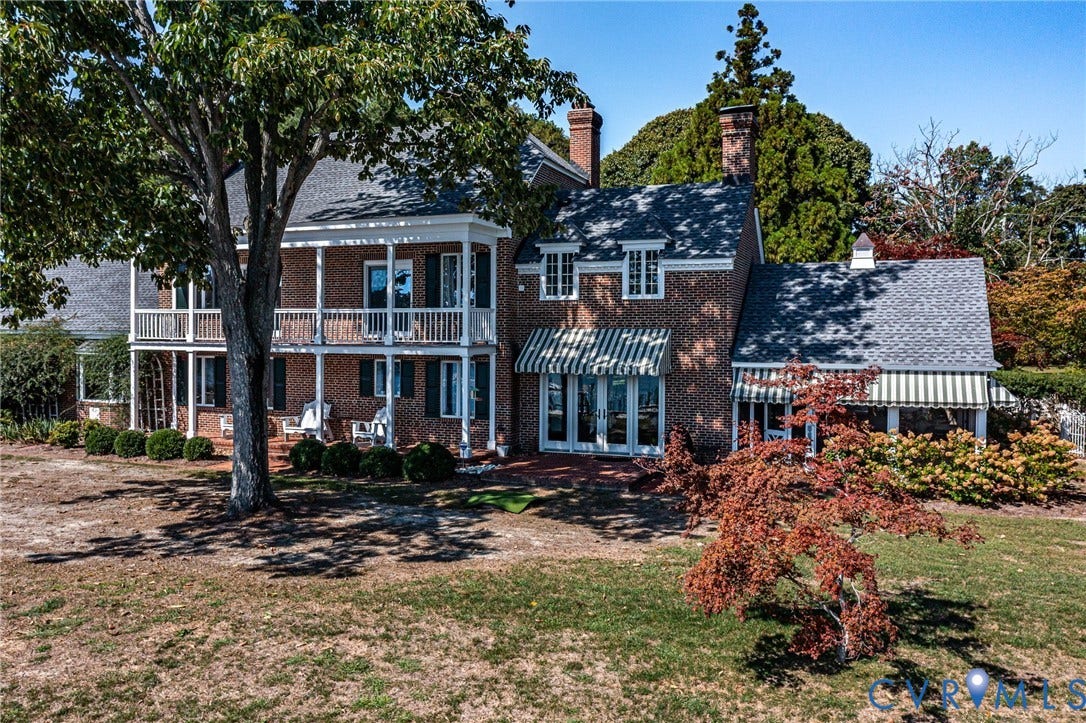 Brick exterior featuring a two-story porch with white railings, striped awnings, and dormer windows