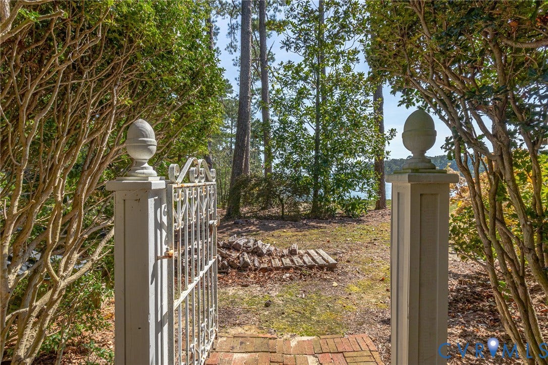 Decorative metal gate with brick paver entrance and mature landscaping
