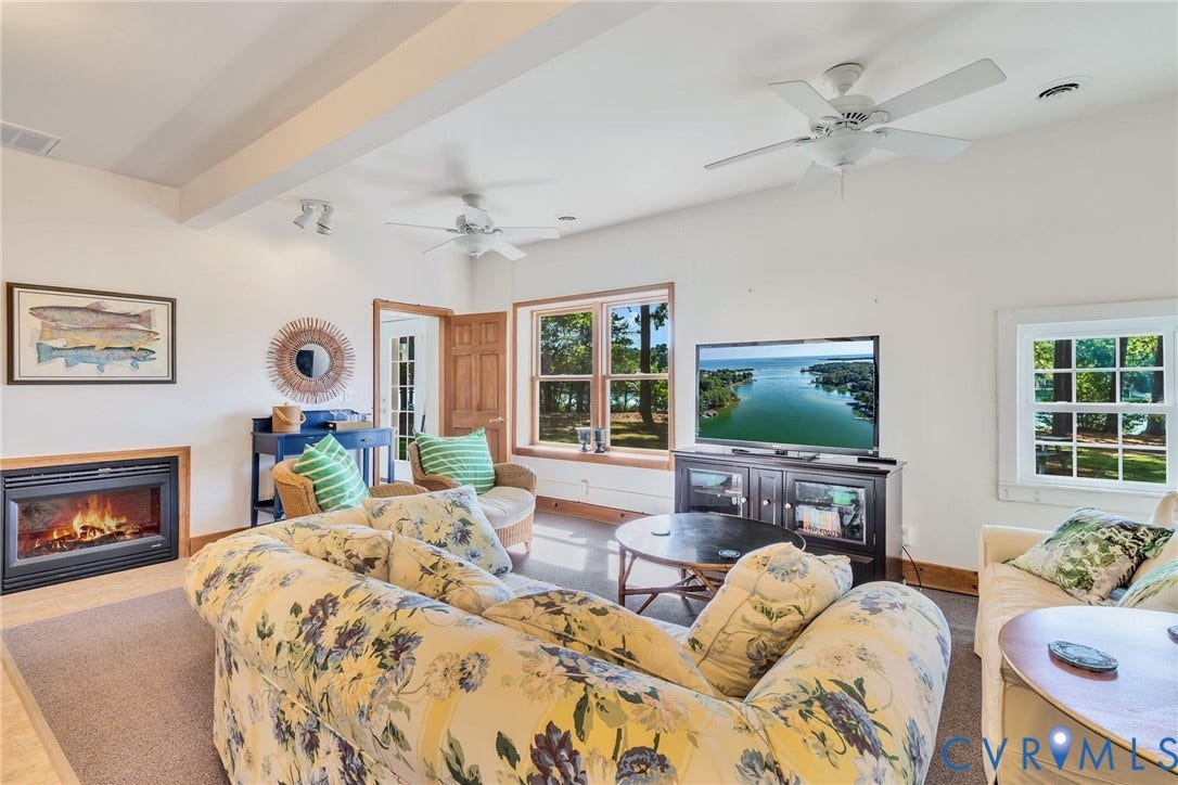 Spacious living area in Guest cottage featuring a built-in fireplace, multiple windows with natural light, exposed ceiling beams, and ceiling fans