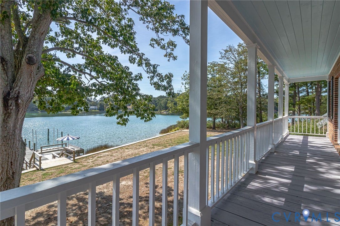 Expansive waterfront porch featuring a pale blue painted ceiling, white wooden railings, and a pier with a picnic table and umbrella