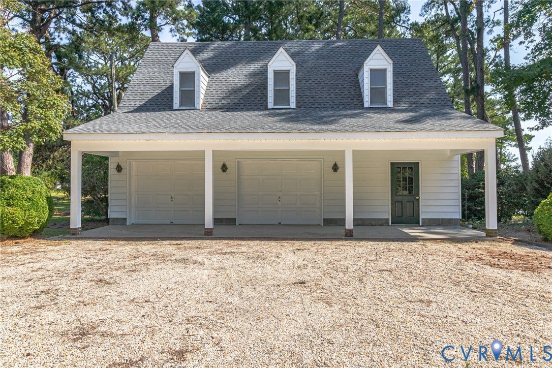 Two-car garage with white paneled doors, covered porch, three dormer windows, and a dark green entry door
