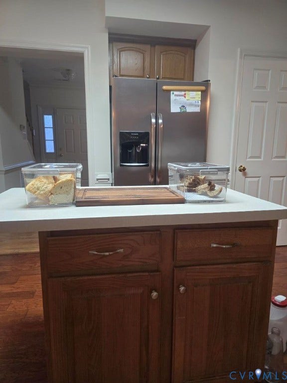 Kitchen island with a light-toned countertop, wood-finish cabinetry, and stainless steel refrigerator