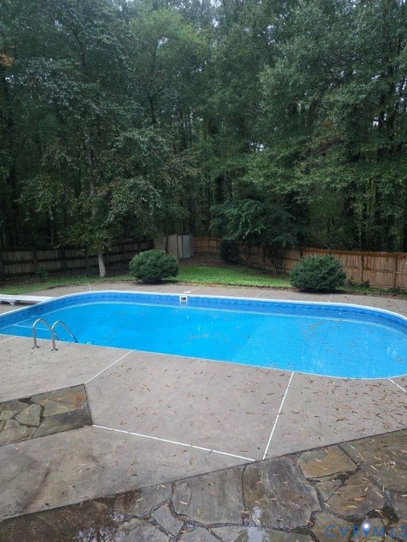 In-ground swimming pool with concrete surround and flagstone accents, surrounded by a wood privacy fence and mature trees