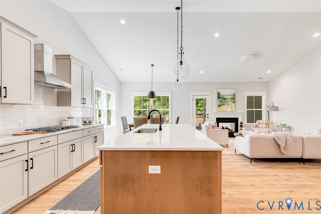 Open-concept design featuring wood-finish flooring, a kitchen island with pendant lighting, a gas range with an exhaust hood, and a fireplace with a mantel