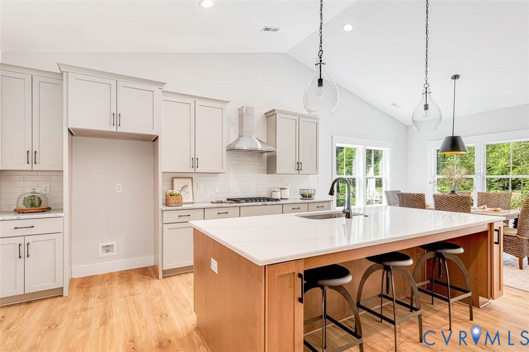 Kitchen featuring wood-finish flooring, light-toned cabinetry, stainless steel range hood, white subway tile backsplash, and a central island with countertop seating