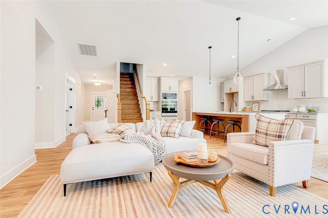Vaulted ceilings, wood-finish flooring, staircase with wood treads, kitchen with light cabinetry, and an island with an integrated breakfast bar