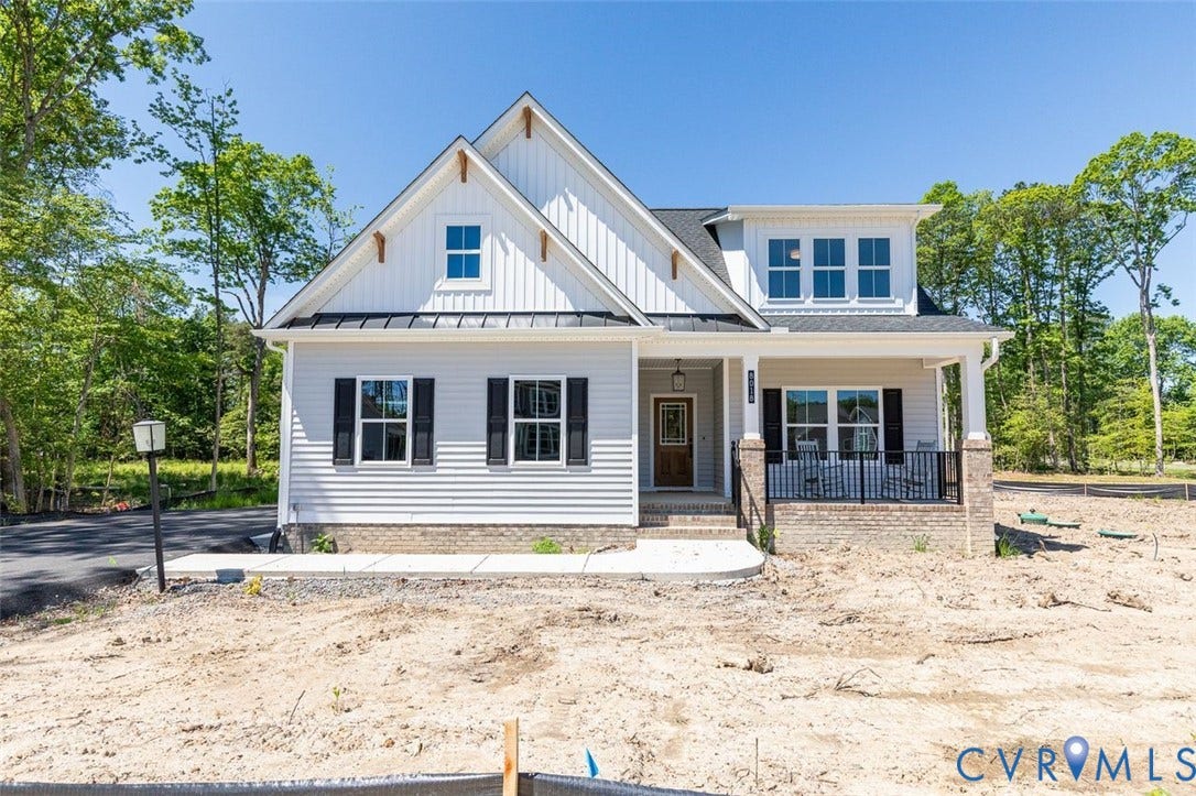 White siding exterior with black shutters, dormer window, covered front porch, and brick foundation accents
