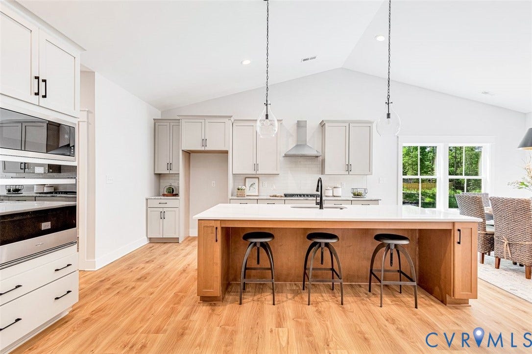 Vaulted ceiling kitchen featuring a large island with white countertop, wood-finish flooring, and stainless steel appliances