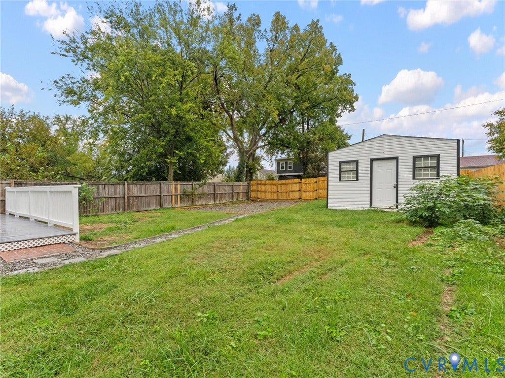 Expansive grassy yard featuring a white-sided shed with black trim windows, a wood fence perimeter, and a white-railed deck