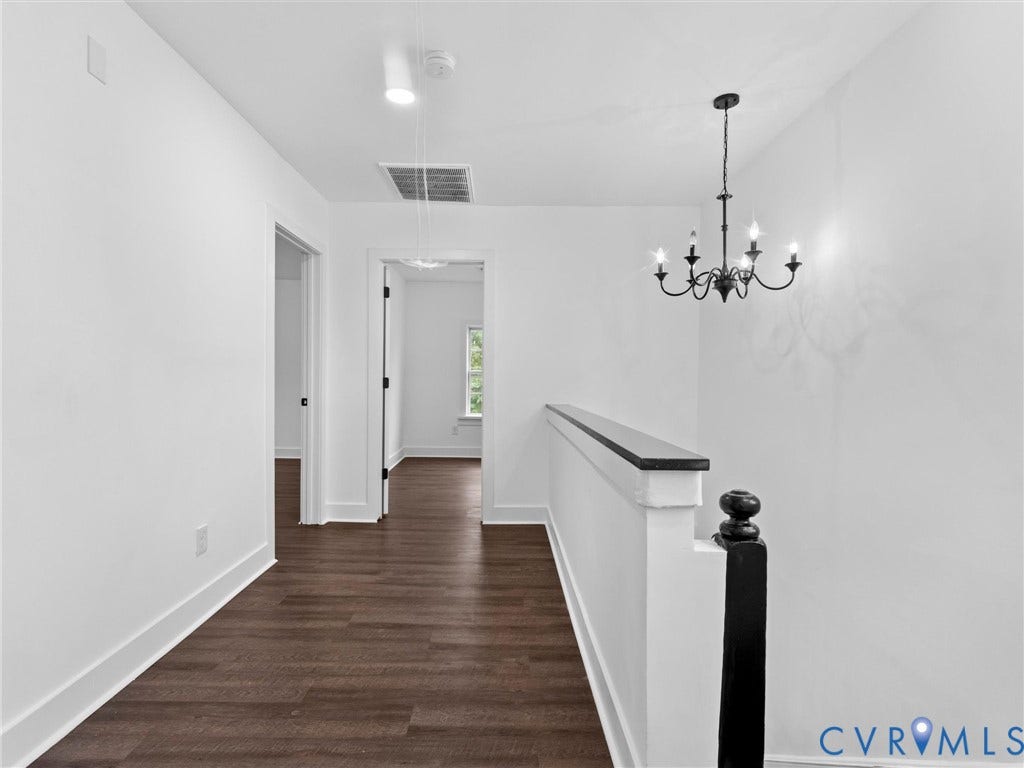 White walls, dark wood-finish flooring, and a black chandelier