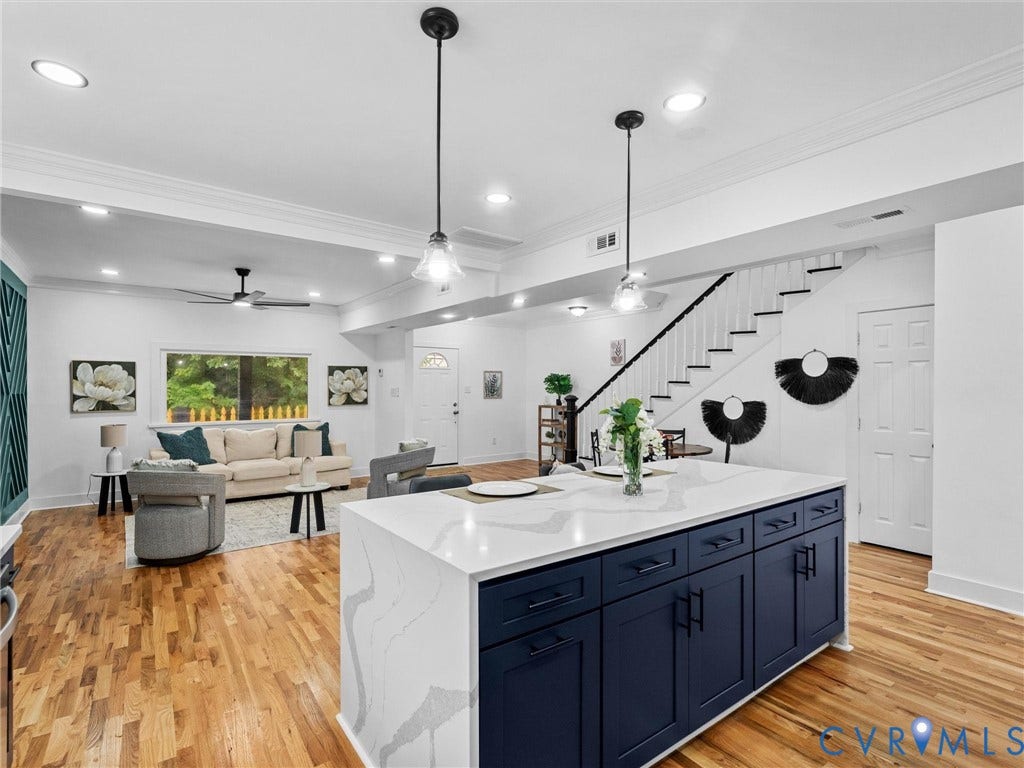 Hardwood-finish flooring throughout, kitchen island with dark blue cabinetry and light-toned countertop, recessed lighting, and a staircase with white risers and dark treads