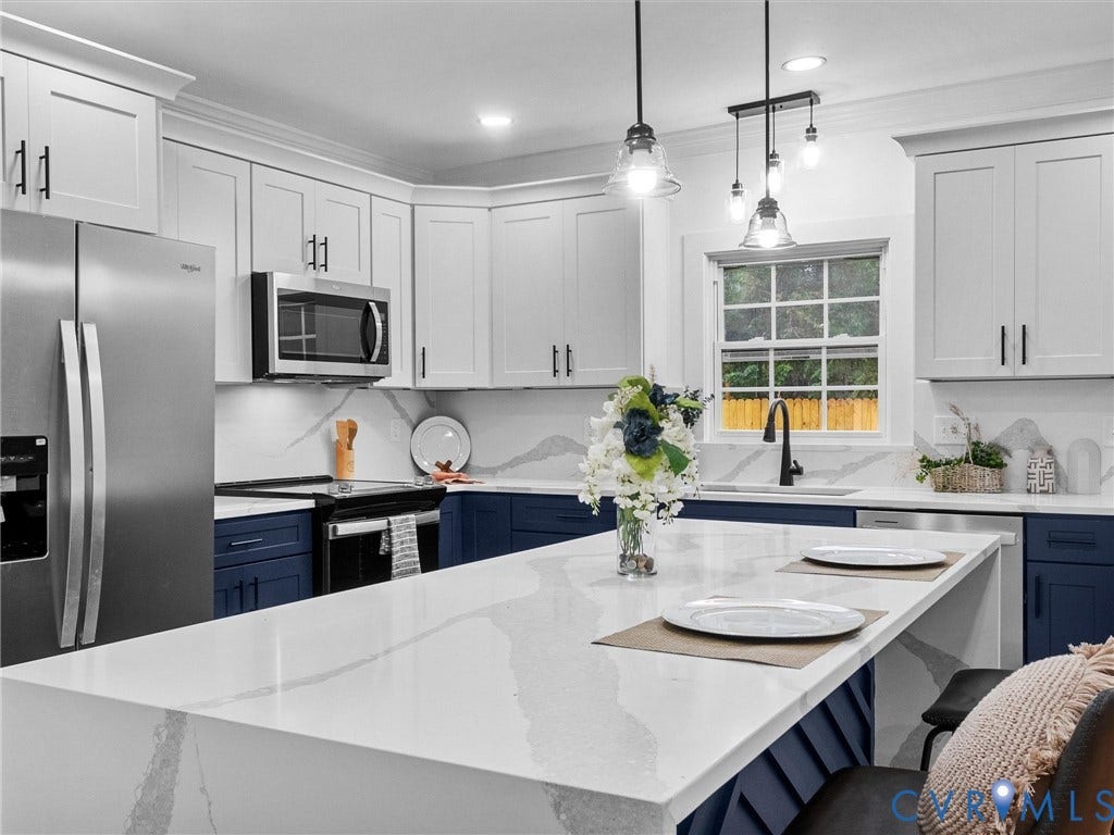 Kitchen featuring stainless steel appliances, solid surface countertops, two-tone cabinetry, and pendant lighting