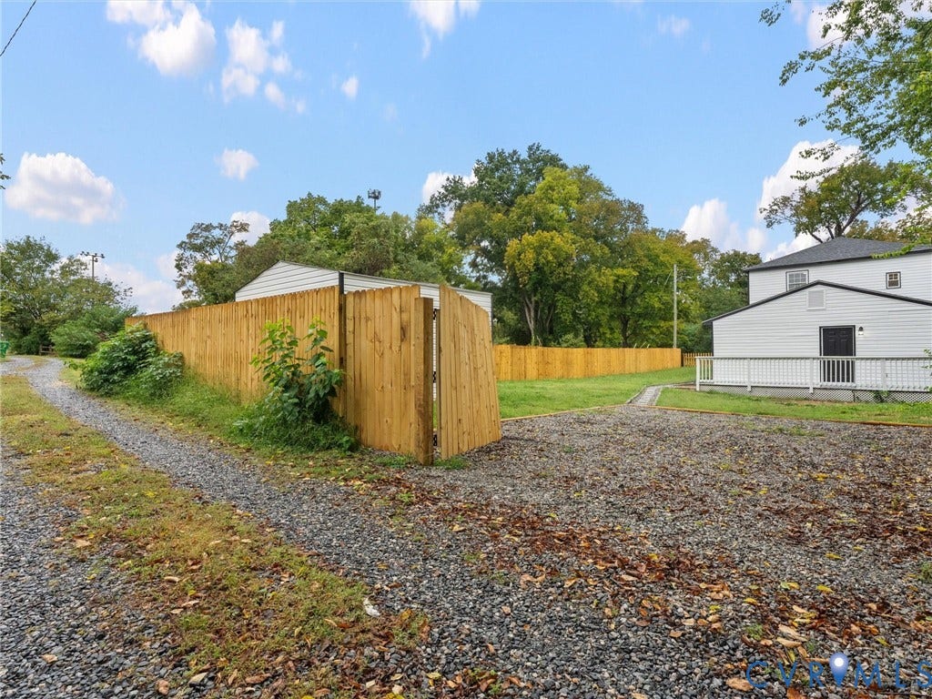 Gravel driveway leading to a wood-plank privacy fence and gate