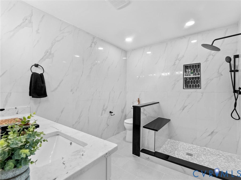 Walk-in shower with a black-framed glass partition, a built-in bench, a rain showerhead, and a tiled niche