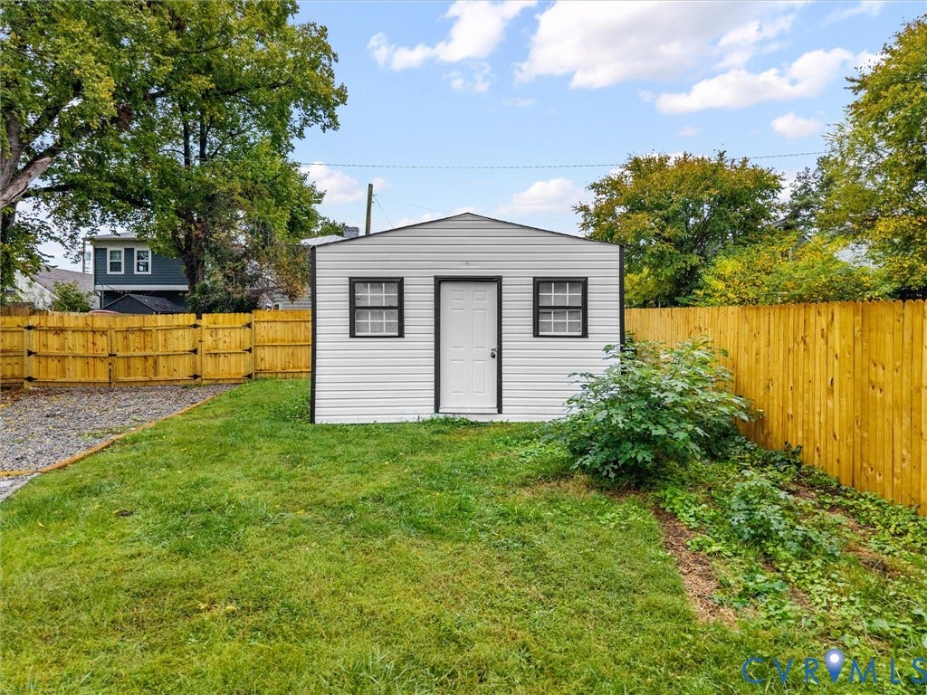 White siding shed with a gabled roof, two windows, and a white entry door