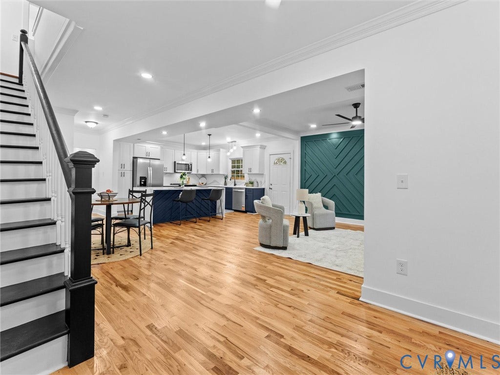 Open-concept living space featuring wood-finish flooring, a contemporary kitchen with a large island, stainless steel appliances, and a decorative accent wall