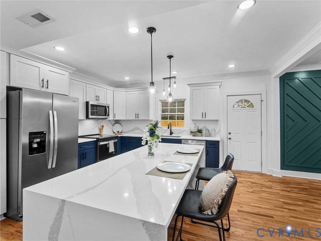 Kitchen featuring a large island with a waterfall edge, stainless steel appliances, two-tone cabinetry, and wood-finish flooring