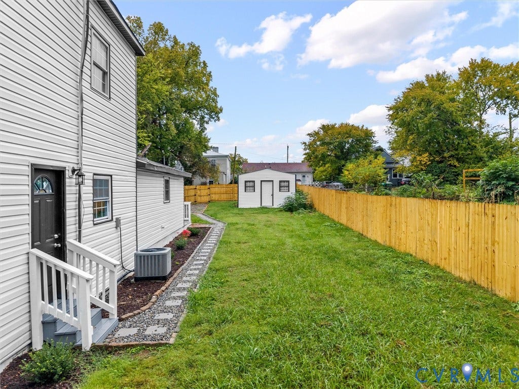 Expansive green lawn with a wood privacy fence, gravel pathway, and an exterior storage shed