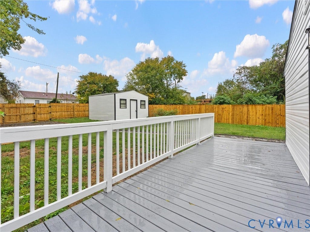 Expansive backyard featuring a wood deck, white railing, and a storage shed