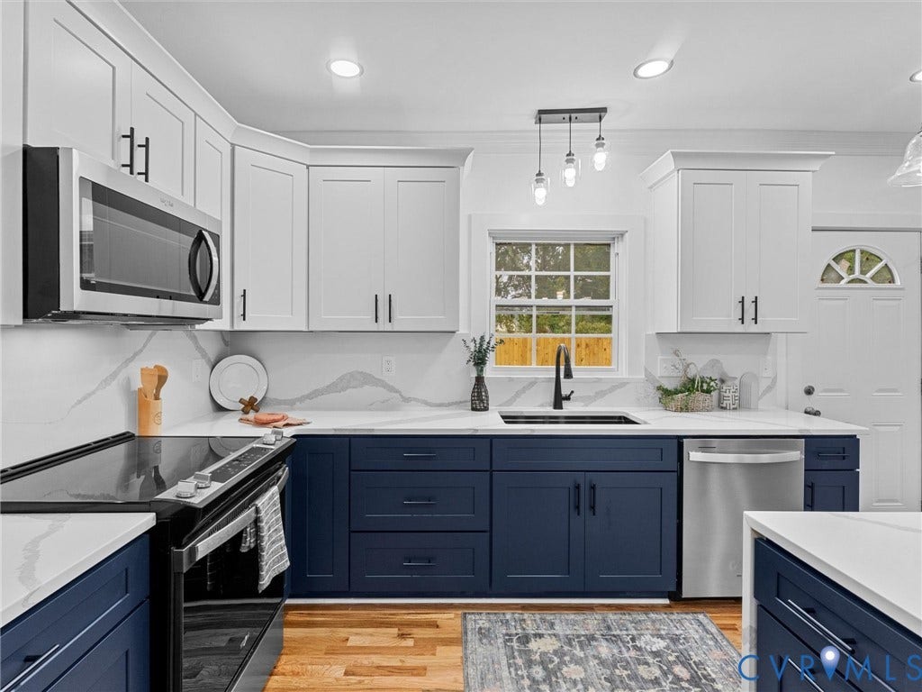 Two-tone cabinetry with white upper and navy lower cabinets, stainless steel appliances, white countertops with veining, and a window above the sink